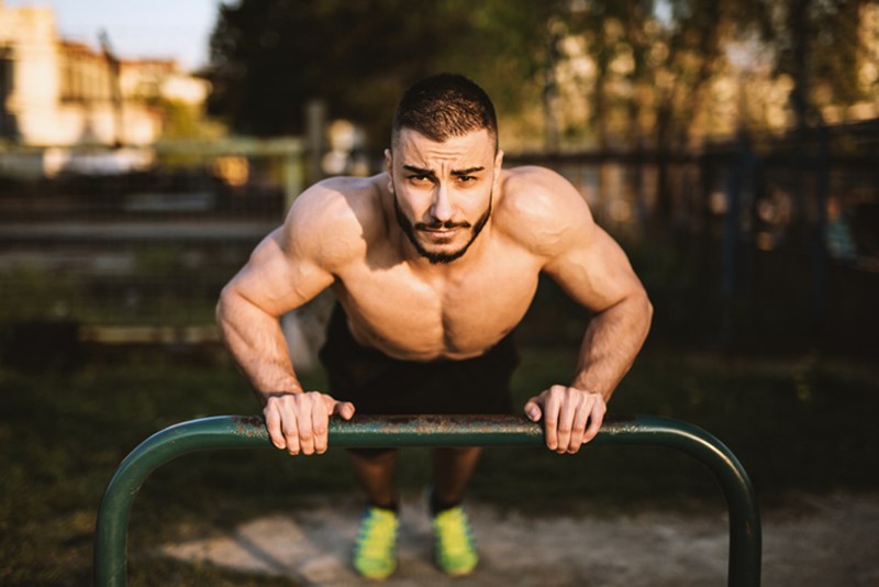YOUNG MAN WORKING ON HIS STRENGTH IN THE LOCAL PARK