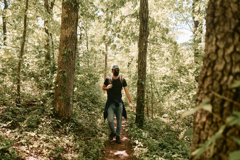 MAN WITH PROTECTIVE FACE MASK WALKING THROUGH A FOREST