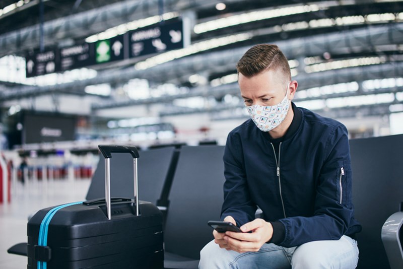 MAN WEARING FACE MASK AND WAITING FOR FLIGHT AT AIRPORT