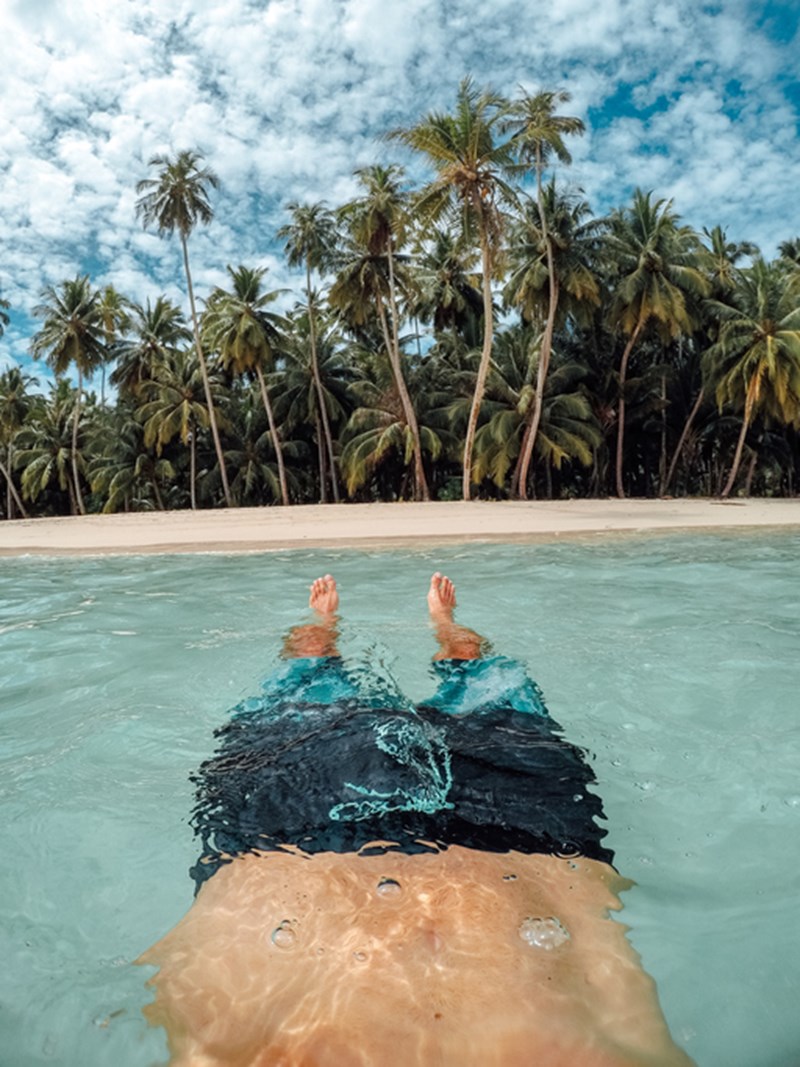 MAN FLOATING IN THE SEA UNDER PALM TREES