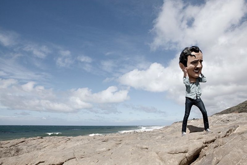 MAN ON THE BEACH HOLDING AN OVERSIZED MASK